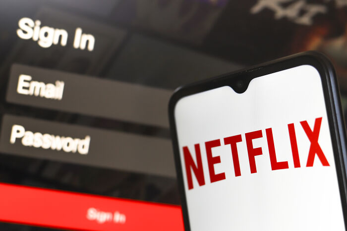 Smartphone displaying Netflix logo in front of a blurred Netflix sign-in screen related to Musk joining Netflix boycott.