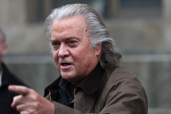 Steve Bannon speaking outdoors, wearing a brown jacket, discussing strategy and a third Trump term in a public setting. Steve Bannon speaking outdoors, wearing a brown jacket, discussing strategy and a third Trump term in a public setting.