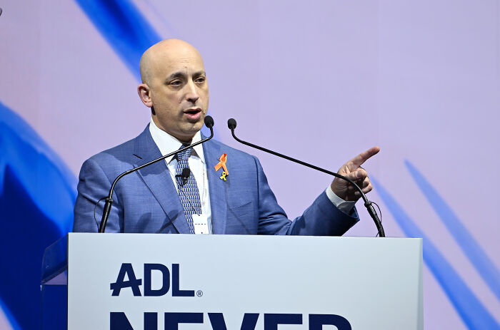 Man in a blue suit speaking at a podium with ADL logo, addressing FBI ties and pro-Israel lobby group involvement.