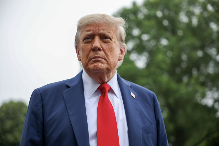Former U.S. president standing outdoors wearing a navy suit and red tie, related to U.S. Navy’s largest aircraft carrier deployment. Former U.S. president standing outdoors wearing a navy suit and red tie, related to U.S. Navy’s largest aircraft carrier deployment.