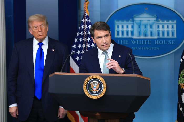 Former President Trump and official at White House podium discussing Trump $230 million compensation bid against DOJ.