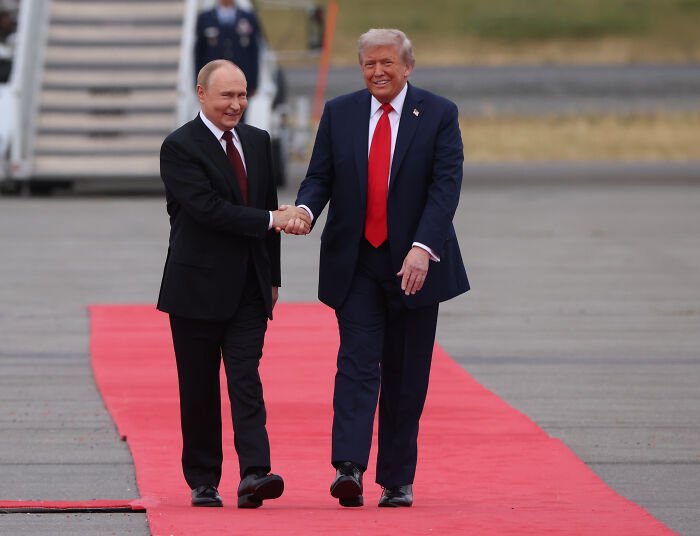 Two men in suits shaking hands on a red carpet, illustrating Karoline Leavitt bizarre text clash with journalist story.