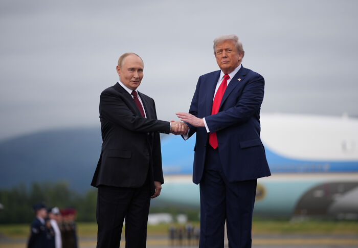 Donald Trump and Vladimir Putin shaking hands outdoors with airplane in background, related to Trump Putin meeting and nuclear tension. Donald Trump and Vladimir Putin shaking hands outdoors with airplane in background, related to Trump Putin meeting and nuclear tension.