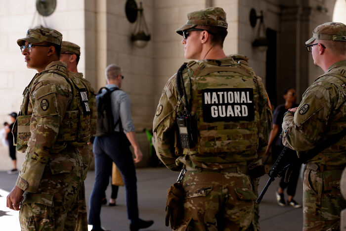 National Guard troops in camouflage uniforms stand alert in a public space, part of Chicago deployment efforts. National Guard troops in camouflage uniforms stand alert in a public space, part of Chicago deployment efforts.