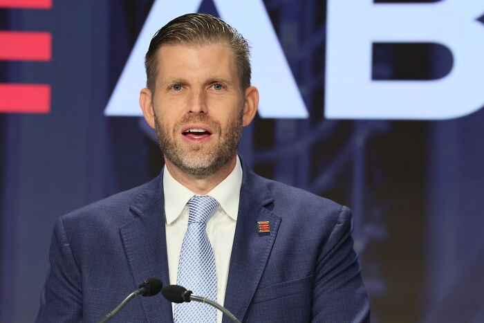 Eric Trump speaking at a podium, wearing a dark suit and blue tie, amid Donald and Melania divorce allegation discussion.