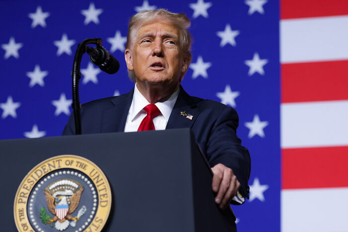 Donald Trump speaking at a podium with U.S. flag backdrop, addressing controversial military training in U.S. cities.