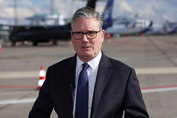 Man in glasses and dark suit standing at airport runway, related to terror attack outside Manchester synagogue on Yom Kippur