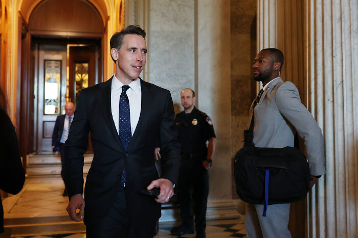 A man in a suit walking through a hallway with security and staff, related to Trump considering paying Americans $2,000.