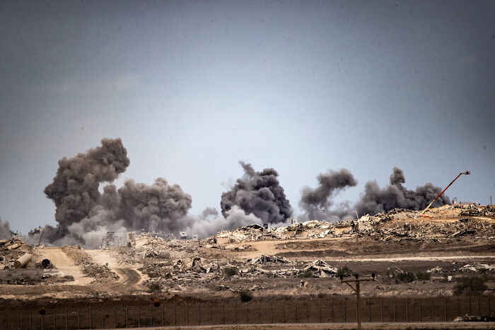 Smoke rising from explosions in a barren landscape amid doubts over Israel’s ceasefire and Hamas hostage situation.