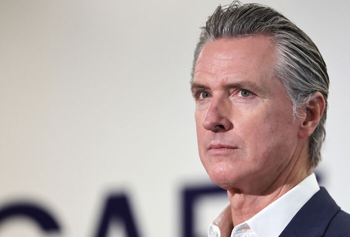 Gavin Newsom in a suit looking serious during a public event, emphasizing fast spreading label for Trump. Gavin Newsom in a suit looking serious during a public event, emphasizing fast spreading label for Trump.
