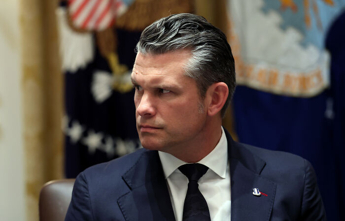 Pete Hegseth in a suit looking serious during a meeting, related to firing fat soldiers after viral Illinois troops photo.