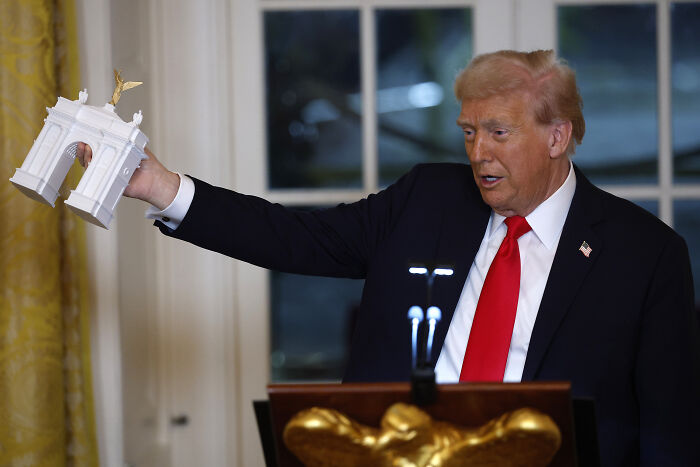 Former President Donald Trump holding a model in a formal setting highlighting government focus during shutdown. Former President Donald Trump holding a model in a formal setting highlighting government focus during shutdown.