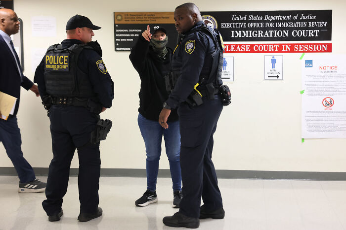 Two police officers in uniforms speaking with a person inside an immigration court, related to mistaken deportation after ICE error. Two police officers in uniforms speaking with a person inside an immigration court, related to mistaken deportation after ICE error.