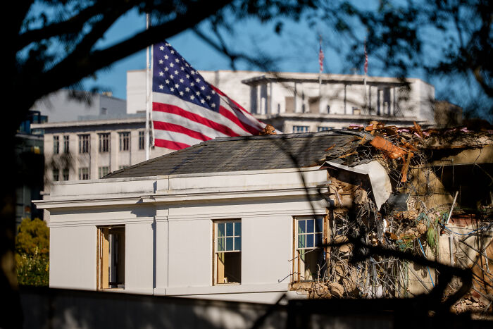Partial demolition of the historic East Wing building with an American flag in the background during Trump’s ballroom project. Partial demolition of the historic East Wing building with an American flag in the background during Trump’s ballroom project.