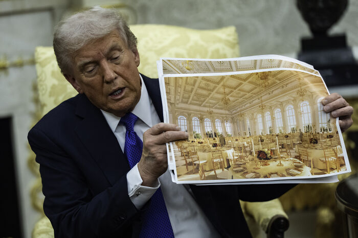 Donald Trump seated, holding a photo of a ballroom, related to historic East Wing demolition and ballroom project plans. Donald Trump seated, holding a photo of a ballroom, related to historic East Wing demolition and ballroom project plans.