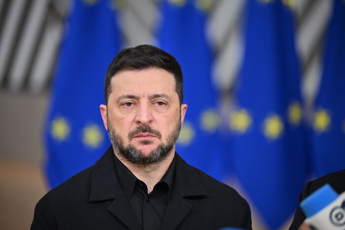 Volodymyr Zelenskyy standing solemnly with European Union flags in the background during a public appearance. Volodymyr Zelenskyy standing solemnly with European Union flags in the background during a public appearance.