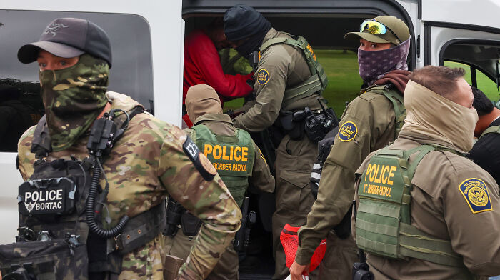 Border Patrol police in tactical gear escort detainees into a van during an ICE operation involving mistaken deportation. Border Patrol police in tactical gear escort detainees into a van during an ICE operation involving mistaken deportation.