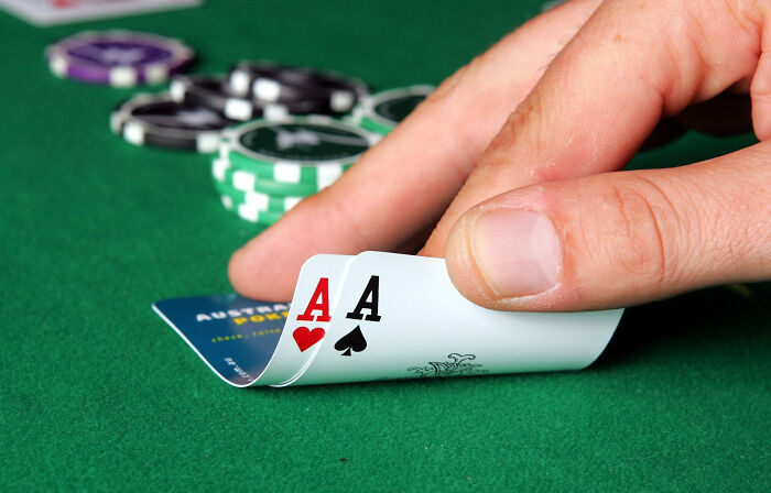 Hand holding two aces on a poker table with chips nearby, illustrating NBA gambling cases involving insider bets and rigged games. Hand holding two aces on a poker table with chips nearby, illustrating NBA gambling cases involving insider bets and rigged games.
