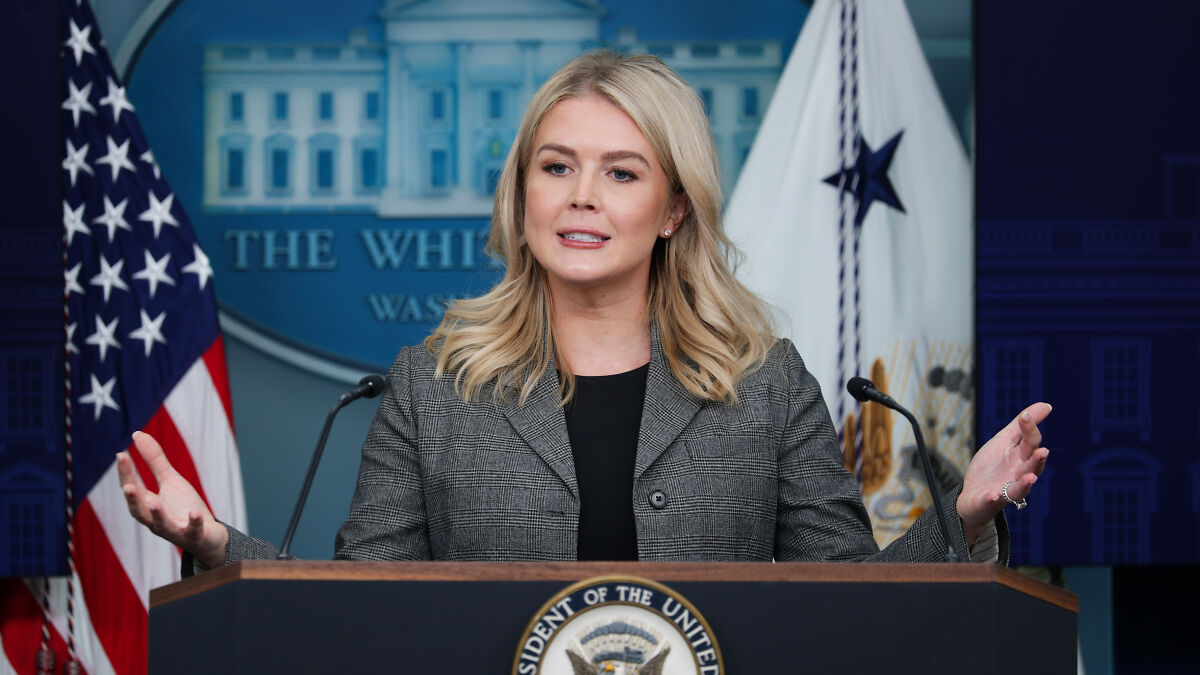 Karoline Leavitt speaking at a podium with US flags in background defending Trumpu2019s AI Medbed video transparency.