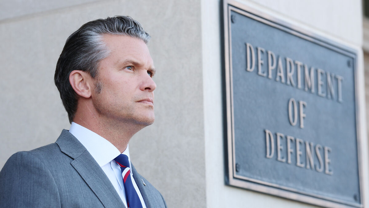 Man in a suit standing outside the Department of Defense building, reflecting on 2025 as a dress rehearsal for a dark chapter.