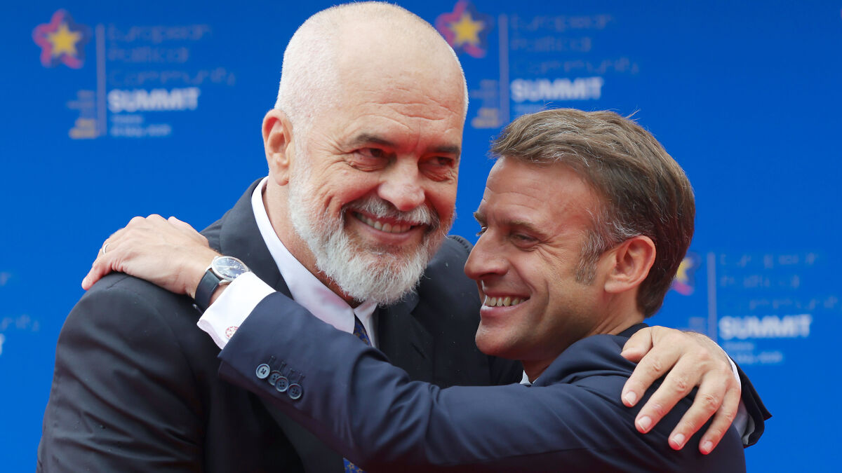 Two European leaders smiling and hugging at a summit, with Donald Trump butt of the joke over geographic gaffe.