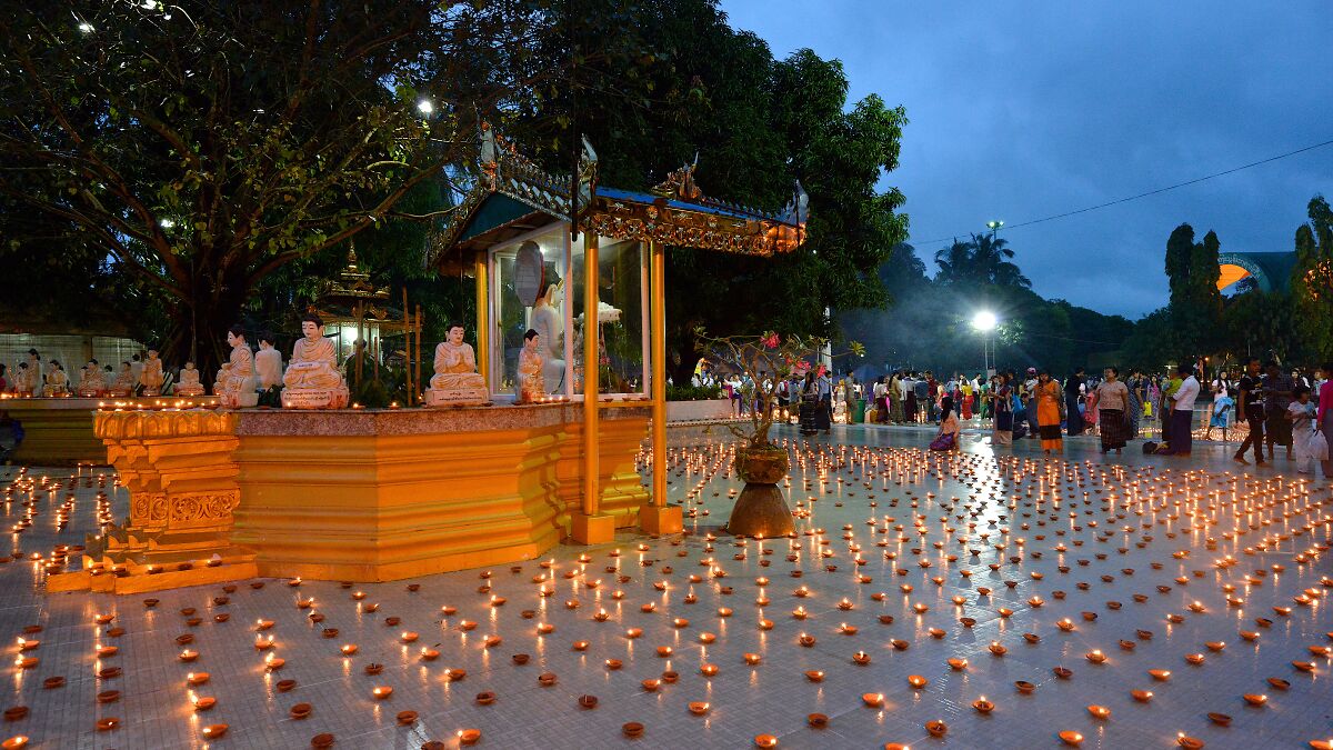 Festival scene at dusk with numerous lit candles, people gathered near statues, unrelated to paraglider bomb incident.