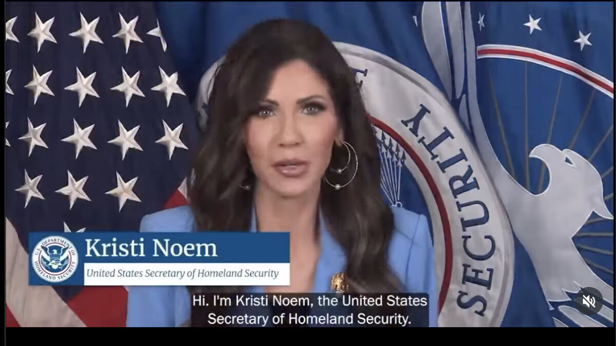 Kristi Noem speaking as United States Secretary of Homeland Security with flags in the background at an official setting.
