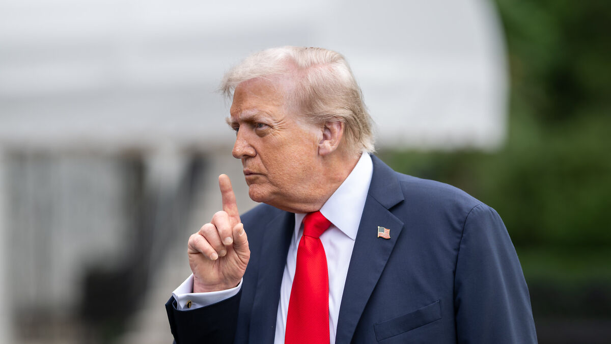 Donald Trump in navy suit and red tie, gesturing with finger raised, reacting to Time Magazine photo and hair controversy.