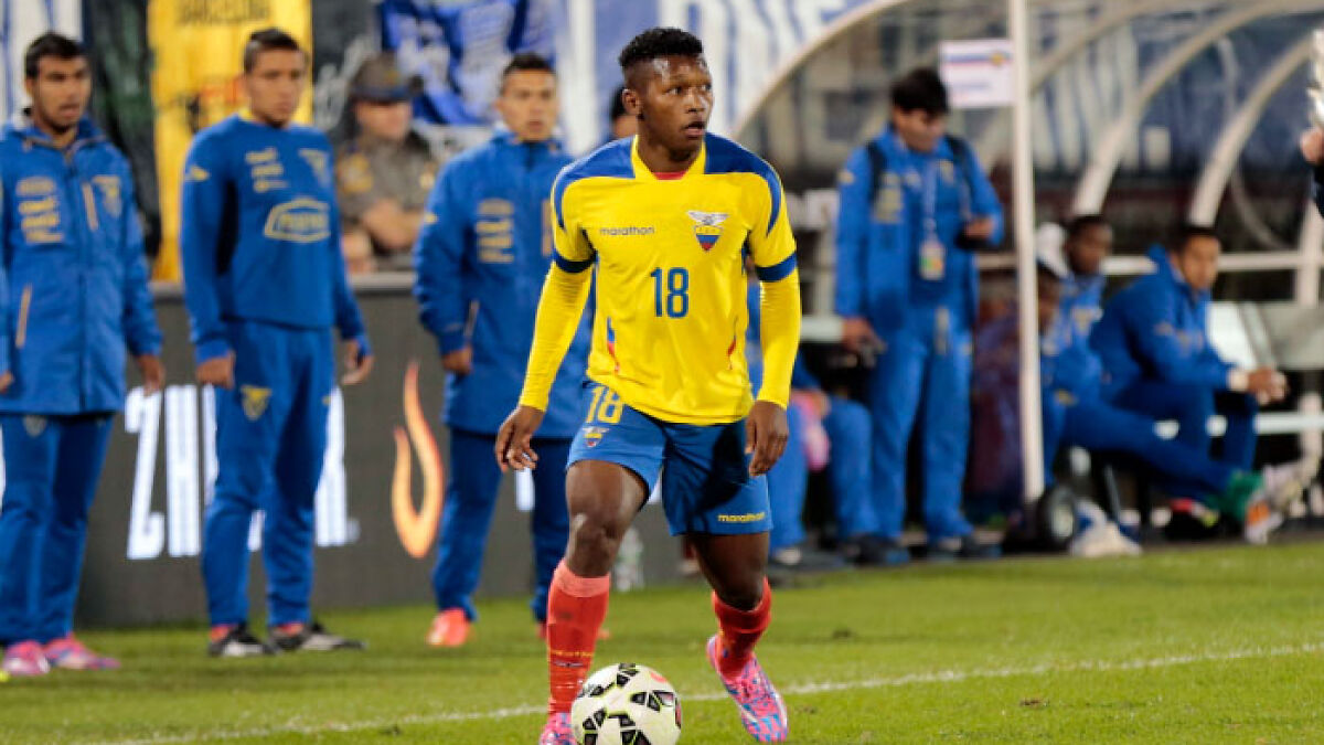 Ecuador soccer player in yellow jersey on the field with team staff in the background during a competitive match.
