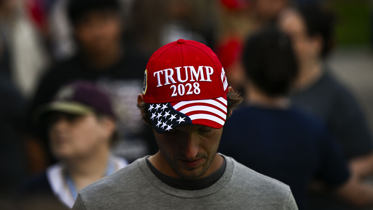 Man wearing red Trump 2028 hat with American flag design suggesting presidency continuation indefinitely in crowd.