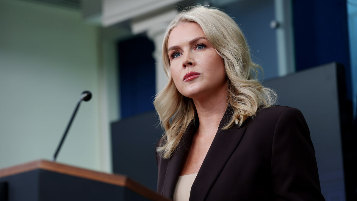 Karoline Leavitt speaking seriously at a podium in a formal setting during a press event or interview.