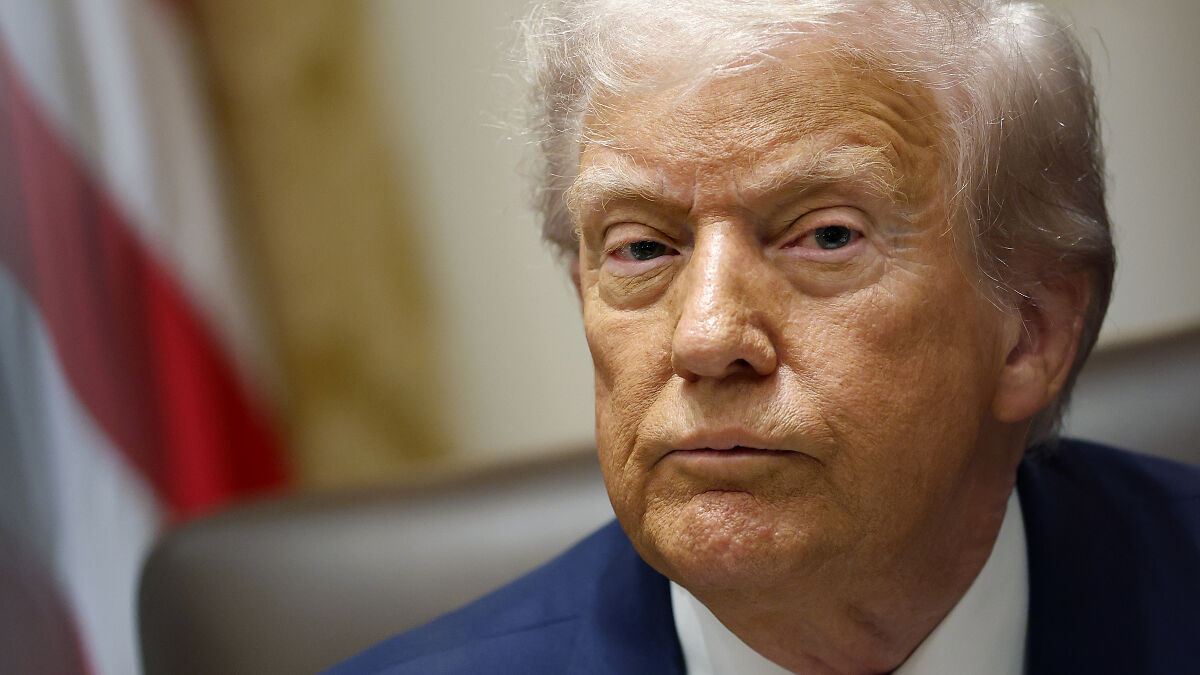Close-up of a serious man with white hair in a suit, with blurred background referencing White House and Trump report.