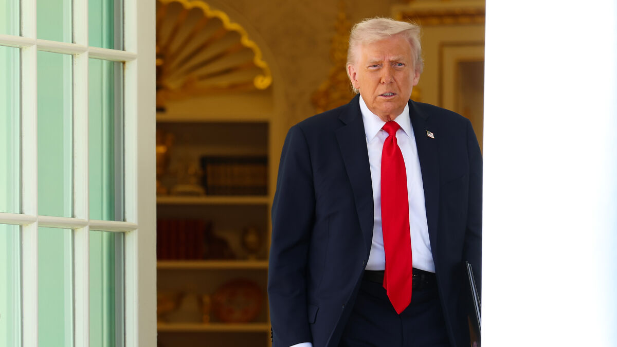 Donald Trump in a dark suit and red tie, standing at a doorway defending $230 million compensation bid against DOJ.