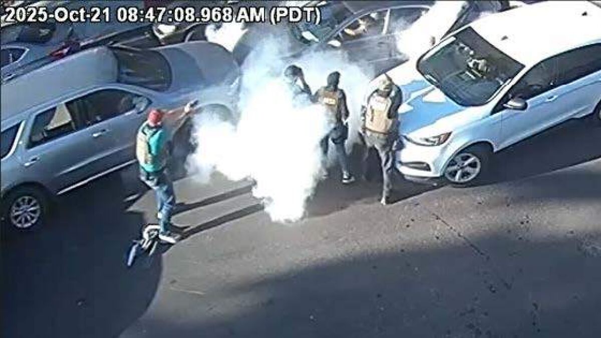 ICE agents in tactical gear during an immigration operation with smoke visible in a parking lot near vehicles