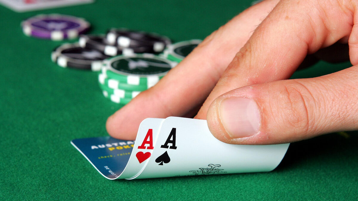 Hand revealing two aces in a poker game with chips on a green table, representing NBA gambling cases and insider bets.
