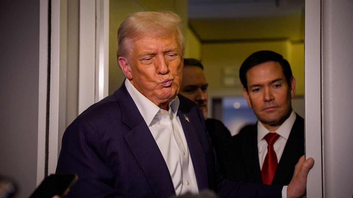Donald Trump in a suit with a pursed expression, standing by a doorway with two men behind him, discussing dementia test confusion.