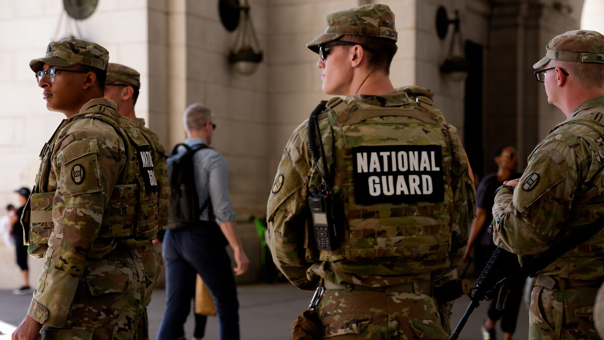 National Guard troops in camouflage gear standing alert in a public urban setting during Chicago deployment preparations.