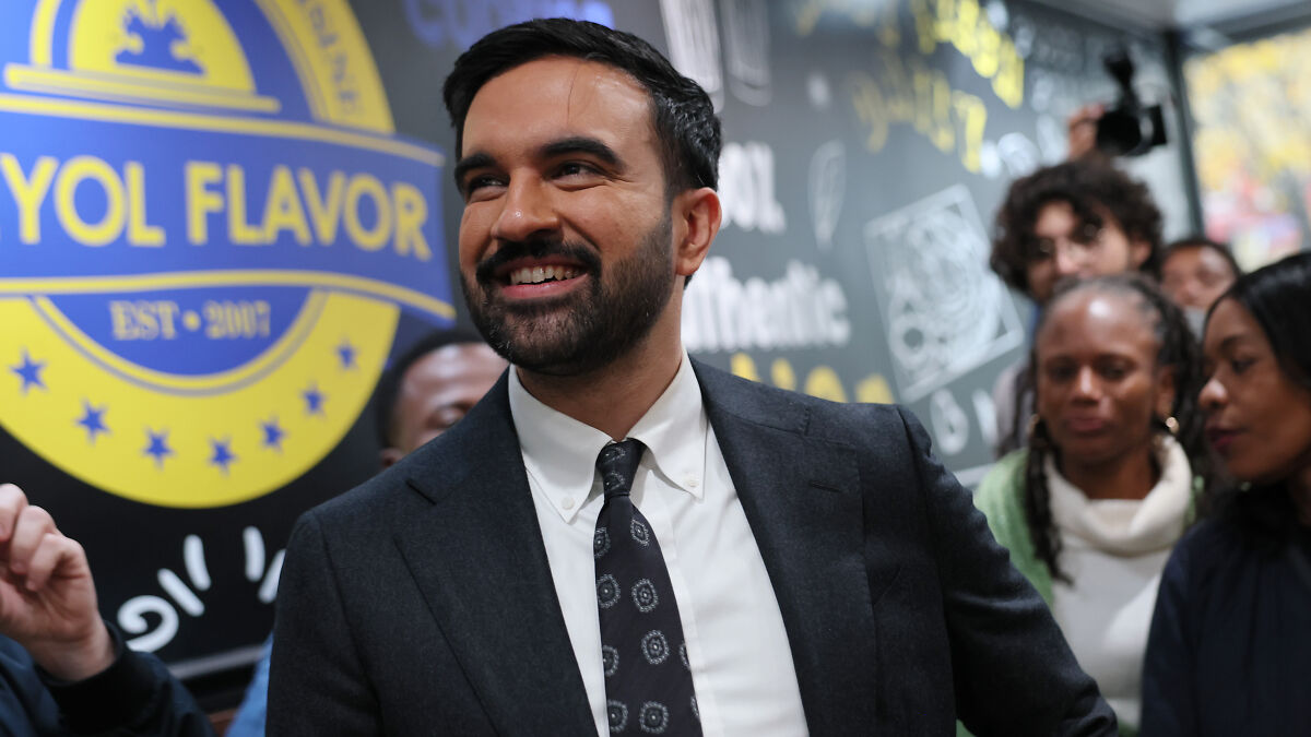 Zohran Mamdani, NYC mayoral frontrunner, smiling in crowd amid discussions of alleged foreign donations controversy.