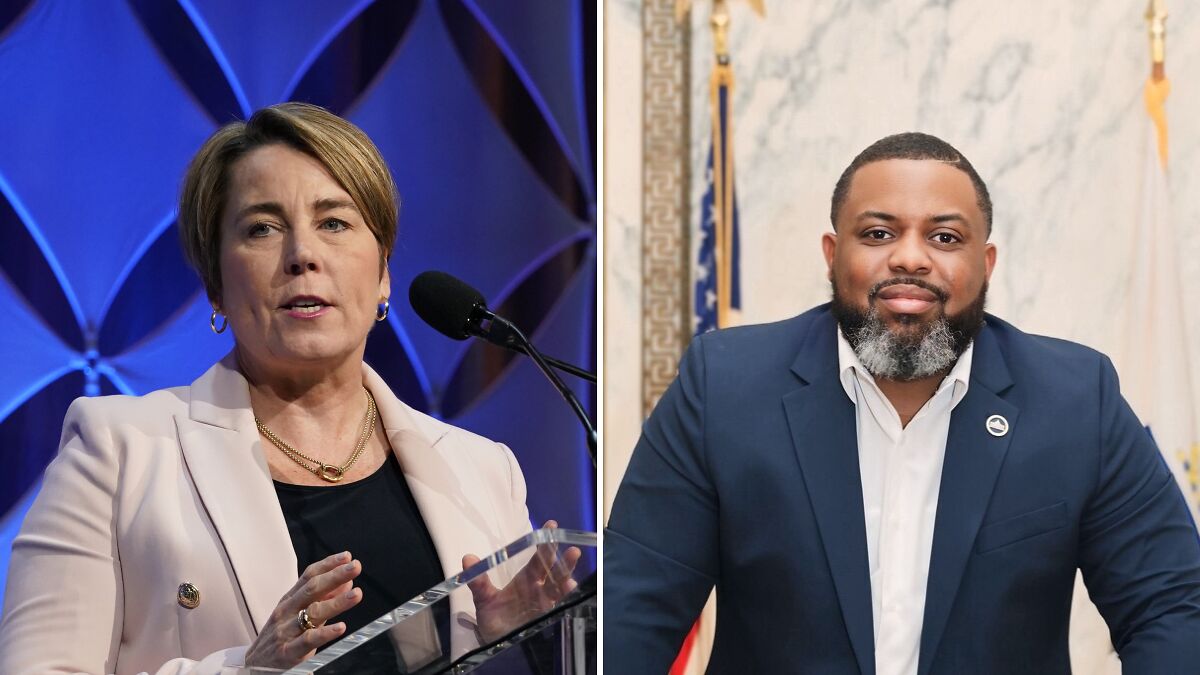 Aide to Gov. Maura Healey speaking at podium and a man in suit in front of flags inside state office building.