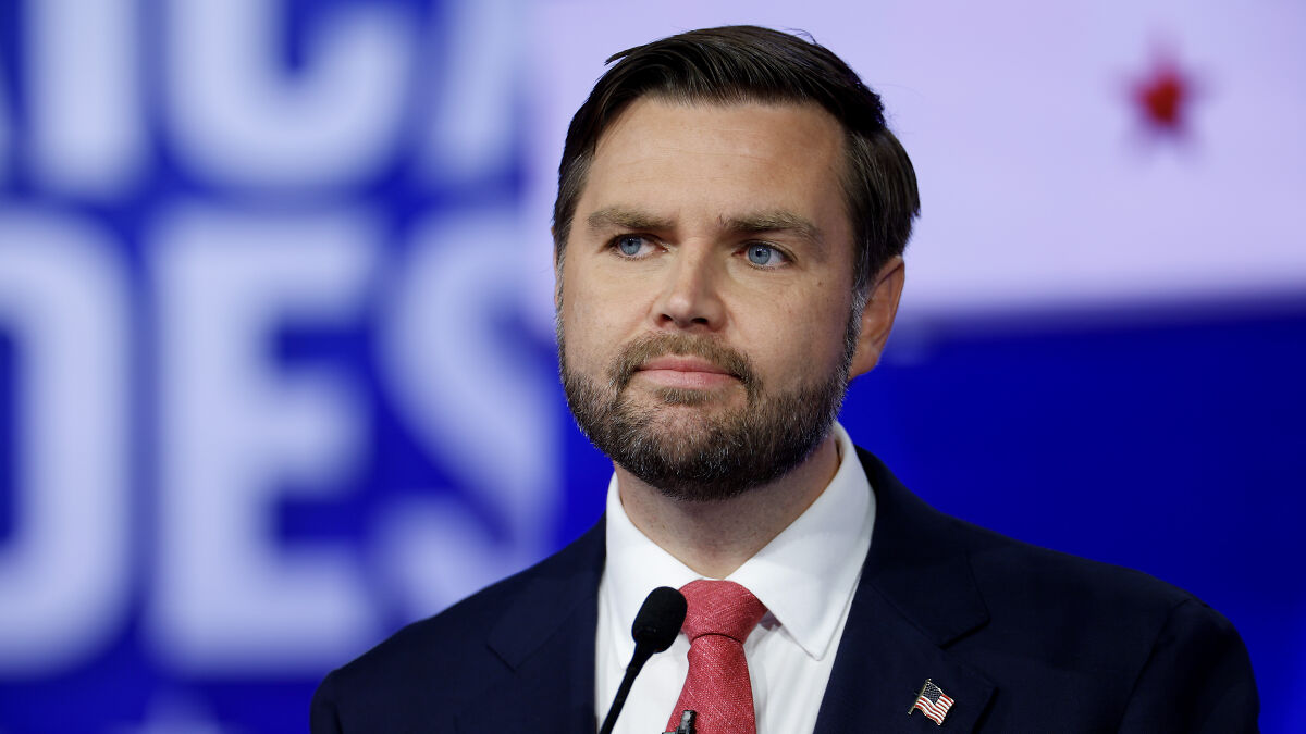 JD Vance speaking at a podium wearing a suit and red tie, discussing Zelenskyy showdown in a formal setting.