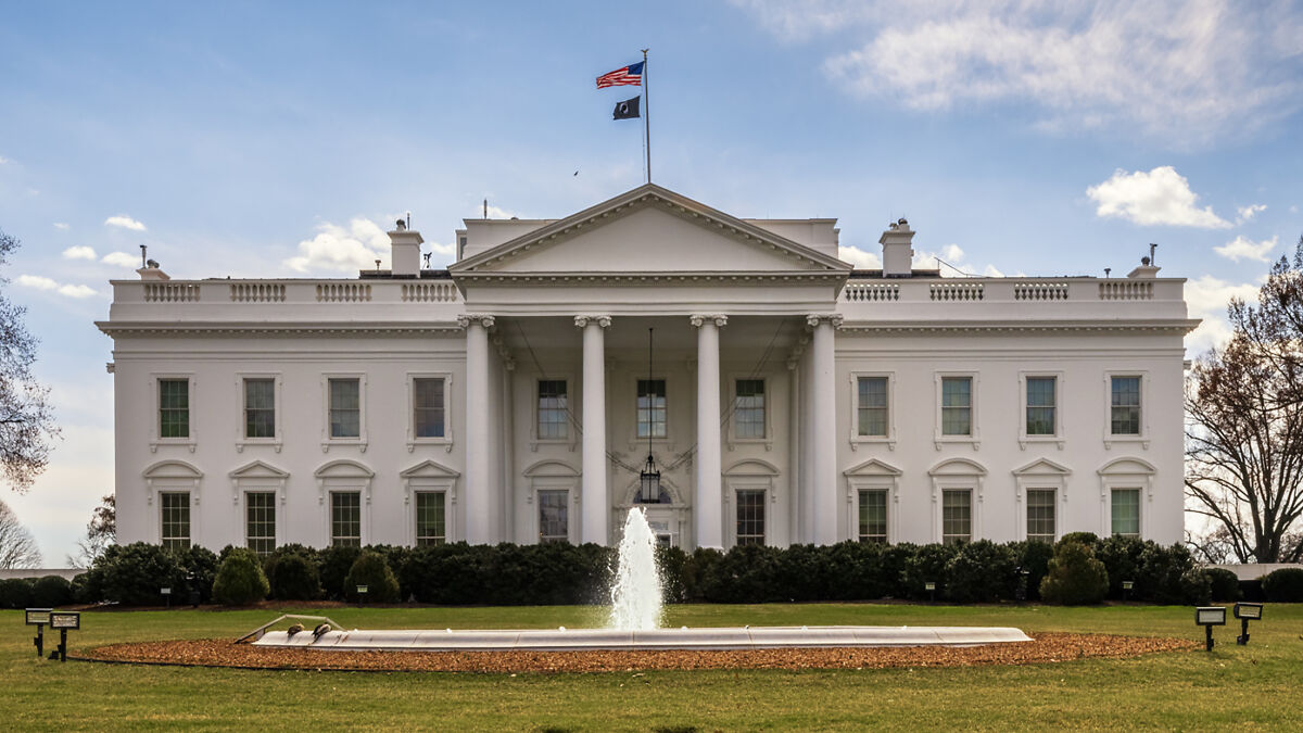 The White House facade with flags flying above, representing Trump supporter and ICE visa issues.