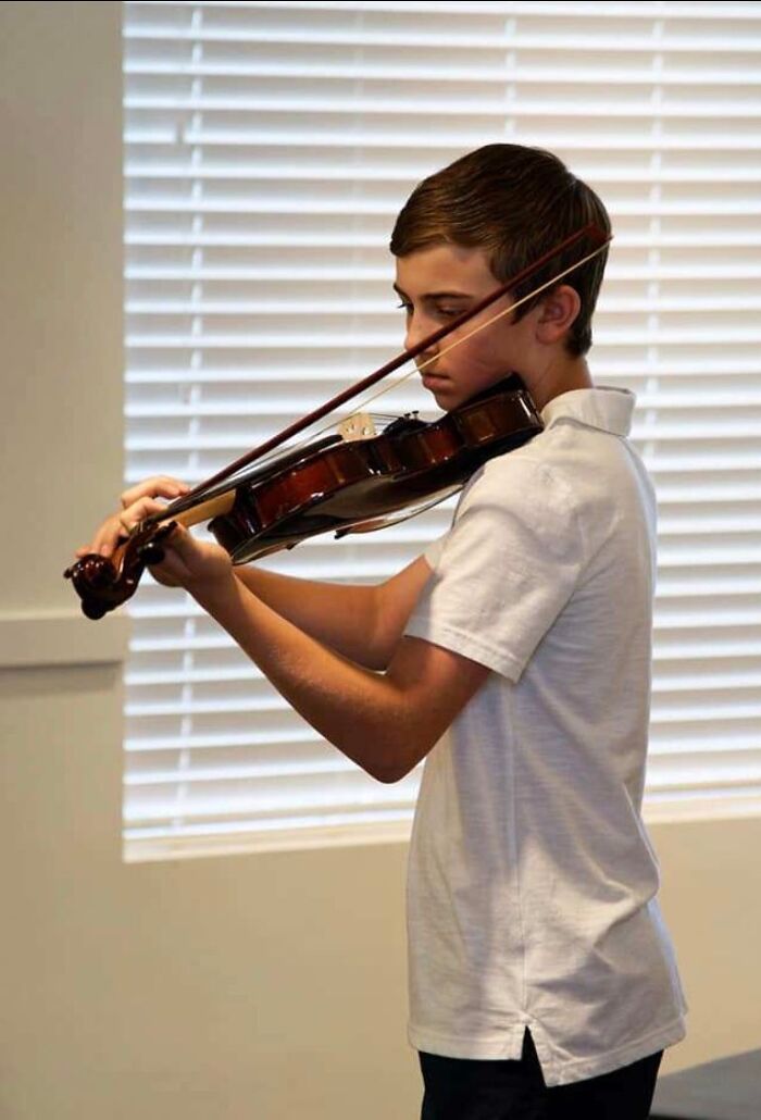 Young boy focused on playing violin indoors with window blinds in the background, related to Florida man case keywords. Young boy focused on playing violin indoors with window blinds in the background, related to Florida man case keywords.
