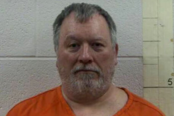 Tennessee man in orange jail uniform with gray hair and beard, detained over Trump meme posted in vigil group. Tennessee man in orange jail uniform with gray hair and beard, detained over Trump meme posted in vigil group.