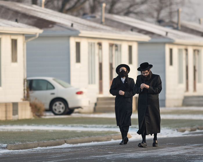 Two men in traditional Lev Tahor sect clothing walk near residential buildings on a cold day during police rescue efforts. Two men in traditional Lev Tahor sect clothing walk near residential buildings on a cold day during police rescue efforts.
