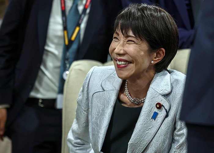 A smiling woman in a silver blazer at a G20 event focusing on new energy and global leadership discussions. A smiling woman in a silver blazer at a G20 event focusing on new energy and global leadership discussions.