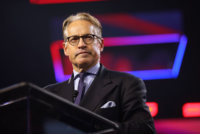 Eric Metaxas speaking at a podium wearing glasses and a suit, reacting to Trump crashing Mar-a-Lago wedding event. Eric Metaxas speaking at a podium wearing glasses and a suit, reacting to Trump crashing Mar-a-Lago wedding event.