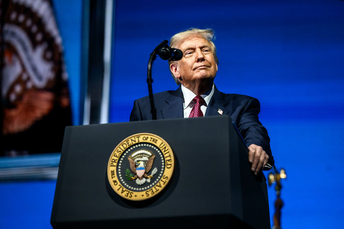 Donald Trump standing at presidential podium during speech with Truth Social AI tool implication. Donald Trump standing at presidential podium during speech with Truth Social AI tool implication.