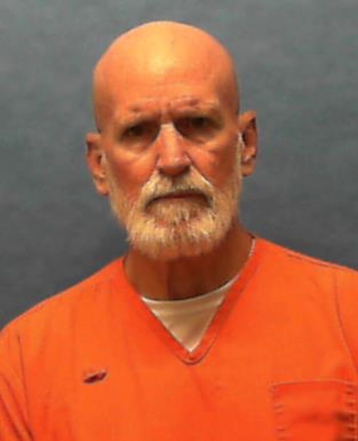 Bald man with white beard wearing an orange prison uniform in a mugshot related to Florida e*******n case.