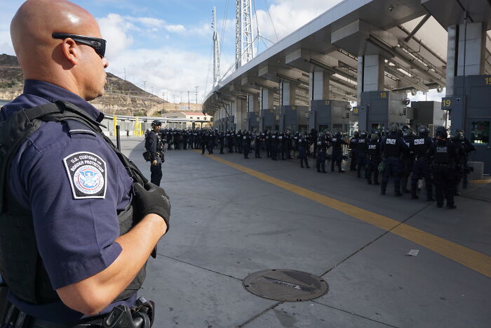 U.S. Border Patrol officers in uniform monitoring a large group during a security operation related to fentanyl supply enforcement. U.S. Border Patrol officers in uniform monitoring a large group during a security operation related to fentanyl supply enforcement.