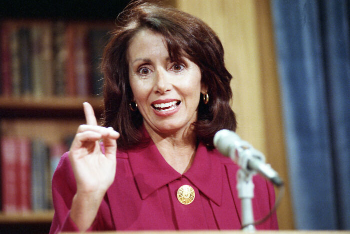 Nancy Pelosi speaking at a podium with a microphone, emphasizing a point during a historic congressional event. Nancy Pelosi speaking at a podium with a microphone, emphasizing a point during a historic congressional event.